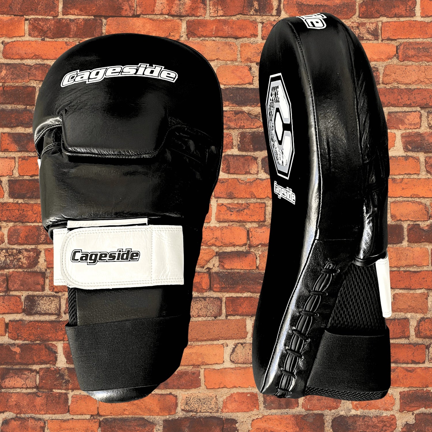 Black Cageside Cobra Focus Mitts against a brick wall background. These durable training mitts are designed with a secure velcro strap and ergonomic hand support for optimal control and precision during striking drills.