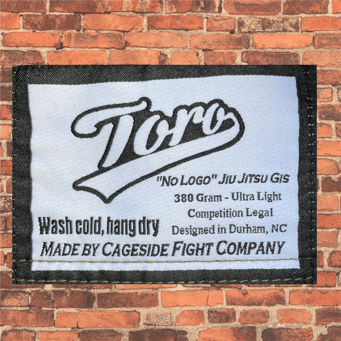 Close-up of the Toro 'No Logo' Jiu-Jitsu Gi tag, highlighting its ultra-light 380-gram fabric, competition-legal design, and made by Cageside Fight Company in Durham, NC. Includes care instructions to wash cold and hang dry.