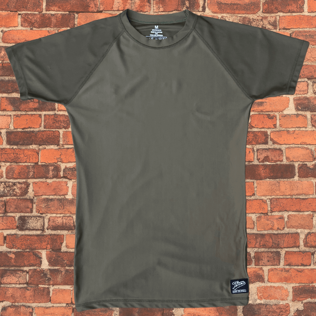 Toro Youth Black Label Olive Drab BJJ Rash Guard laid flat on brick background showing short sleeve design
