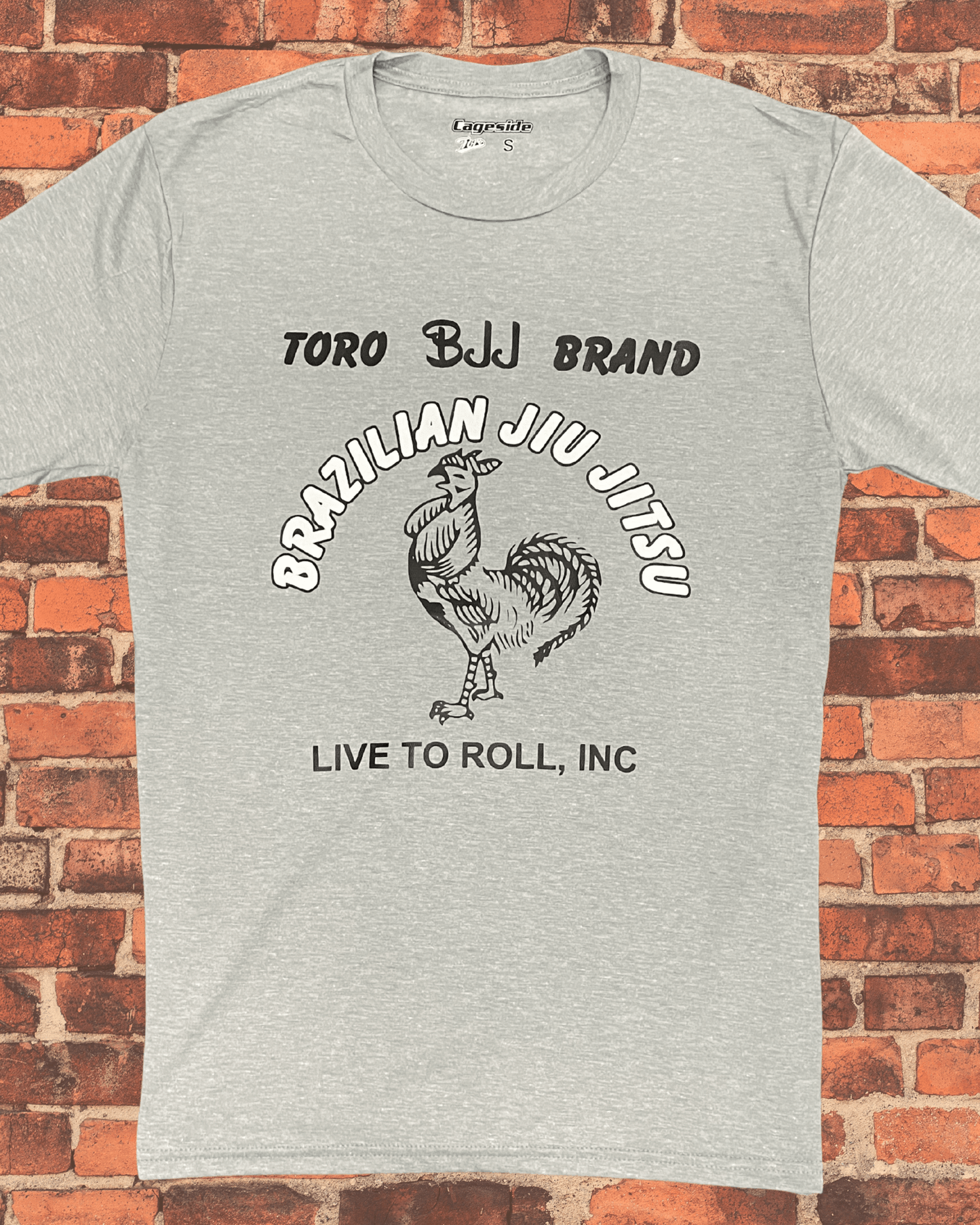A heathered gray Toro BJJ Brand t-shirt featuring a black and white rooster graphic centered between the text "Brazilian Jiu Jitsu" and "Live to Roll, Inc" on a red brick background.