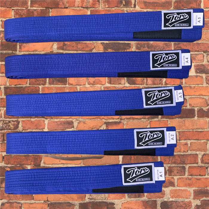 BJJ Blue belts by Toro, cotton construction, black stripe bar, sizes A1 to A5 displayed on brick wall background.