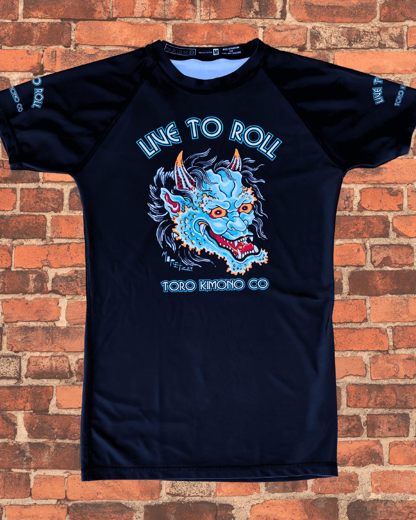 Toro BJJ Green Oni Rash Guard with a bold demon mask design, “Live to Roll” across the chest, and “Toro Kimono Co” printed below.