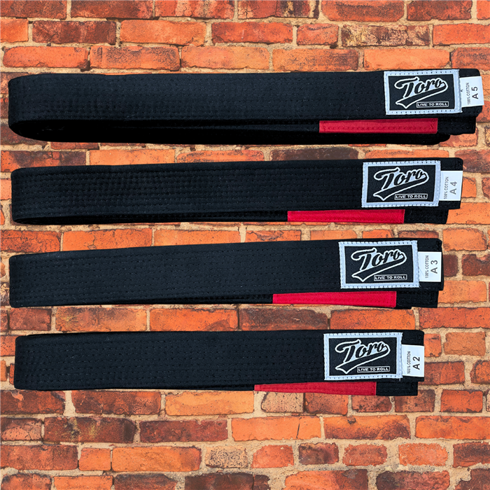 IBJJF-approved black BJJ belts from Toro with red rank bars, displayed in sizes A2 to A5 on a brick wall background.