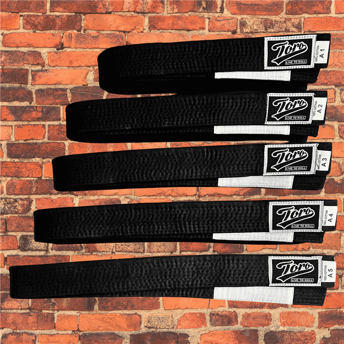 Toro BJJ IBJJF-approved black belt with white bar, available in sizes A1 to A5, displayed on a brick background.