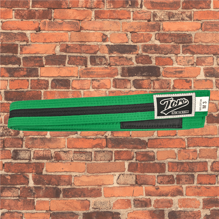 Toro BJJ kids green and black BJJ belts in sizes M000–M5, Toro logo patch with 'Live to Roll' text beneath, black rank bar, brick background.