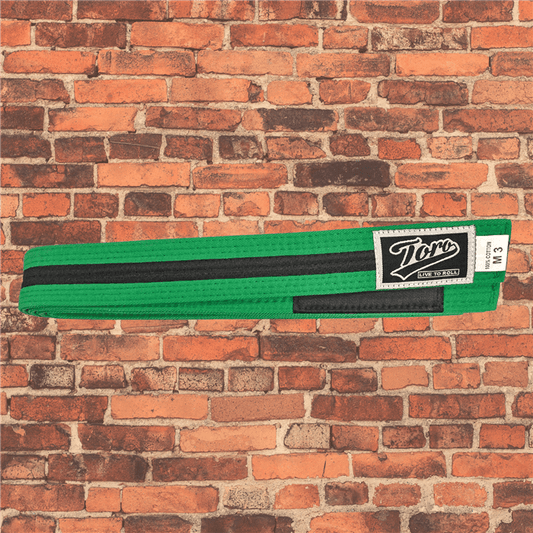 Toro BJJ kids green and black BJJ belts in sizes M000–M5, Toro logo patch with 'Live to Roll' text beneath, black rank bar, brick background.