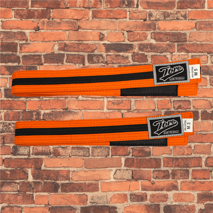 Toro BJJ kids orange and black BJJ belts in sizes M000–M5, featuring black rank bars and Toro logo patches, displayed on a brick background.