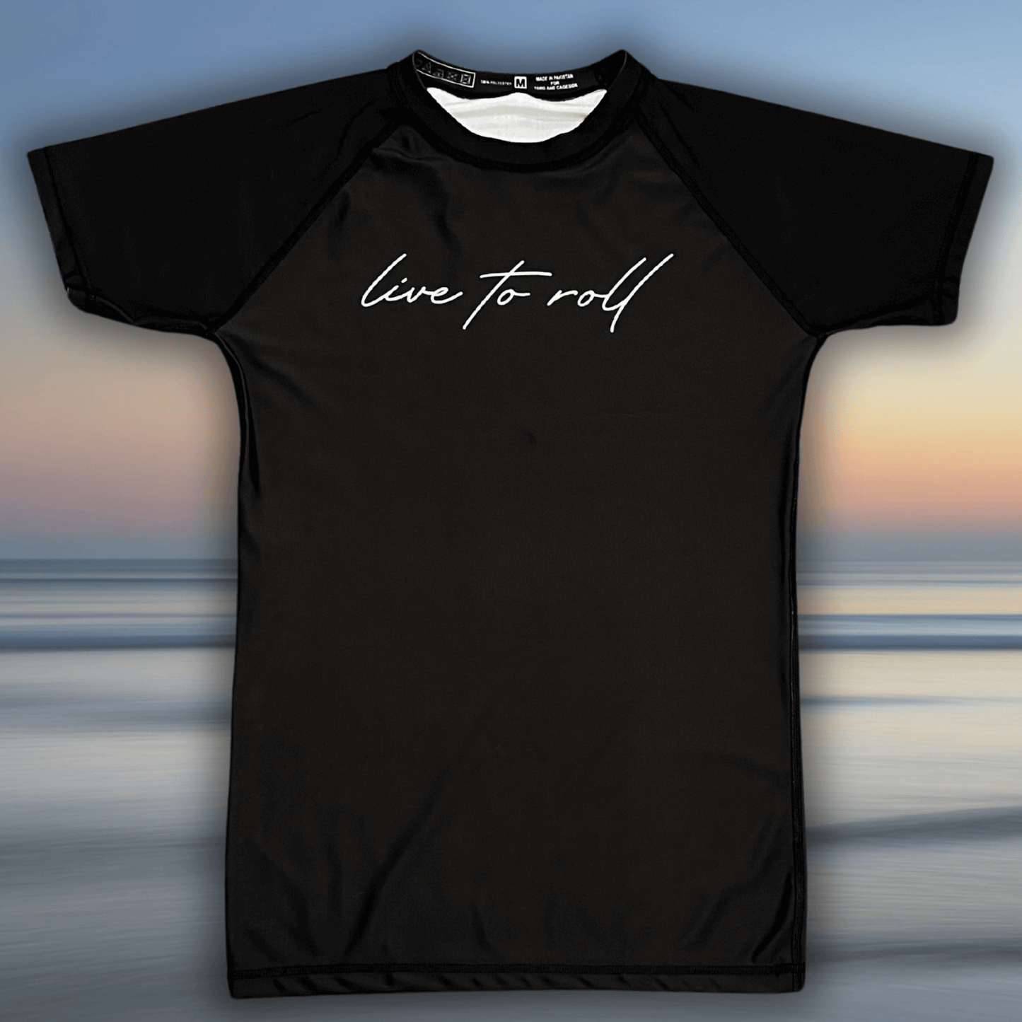 Flat lay of Toro BJJ Live To Roll black short sleeve rash guard with white script text across the chest.