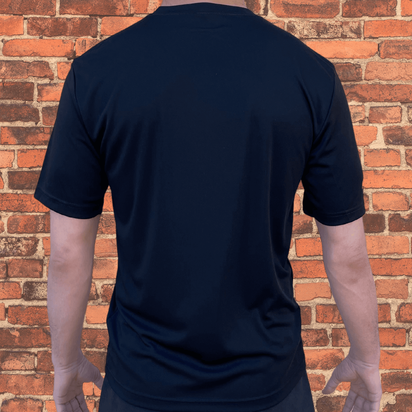 Back view of Toro BJJ Loose Fit Rash Guard in black, plain design, short sleeves, worn by male model, brick wall background.