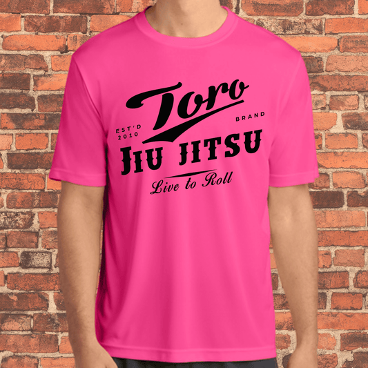 Adult-sized neon pink loose fit rash guard with bold black Toro Jiu Jitsu "Live to Roll" design, worn by a model in front of a brick wall.