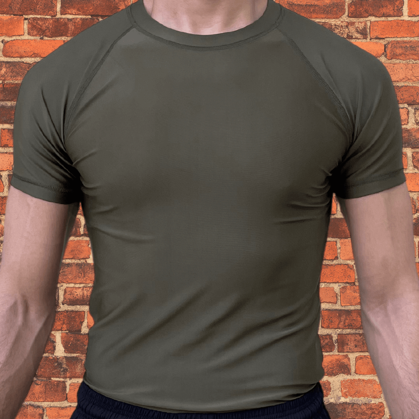 Front view of a plain Toro BJJ Olive Drab Rash Guard with short sleeves and a minimalist design against a brick wall background.
