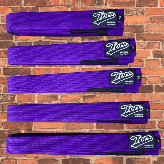 Premium purple BJJ belt with Toro logo patch and black rank bar on a brick wall background