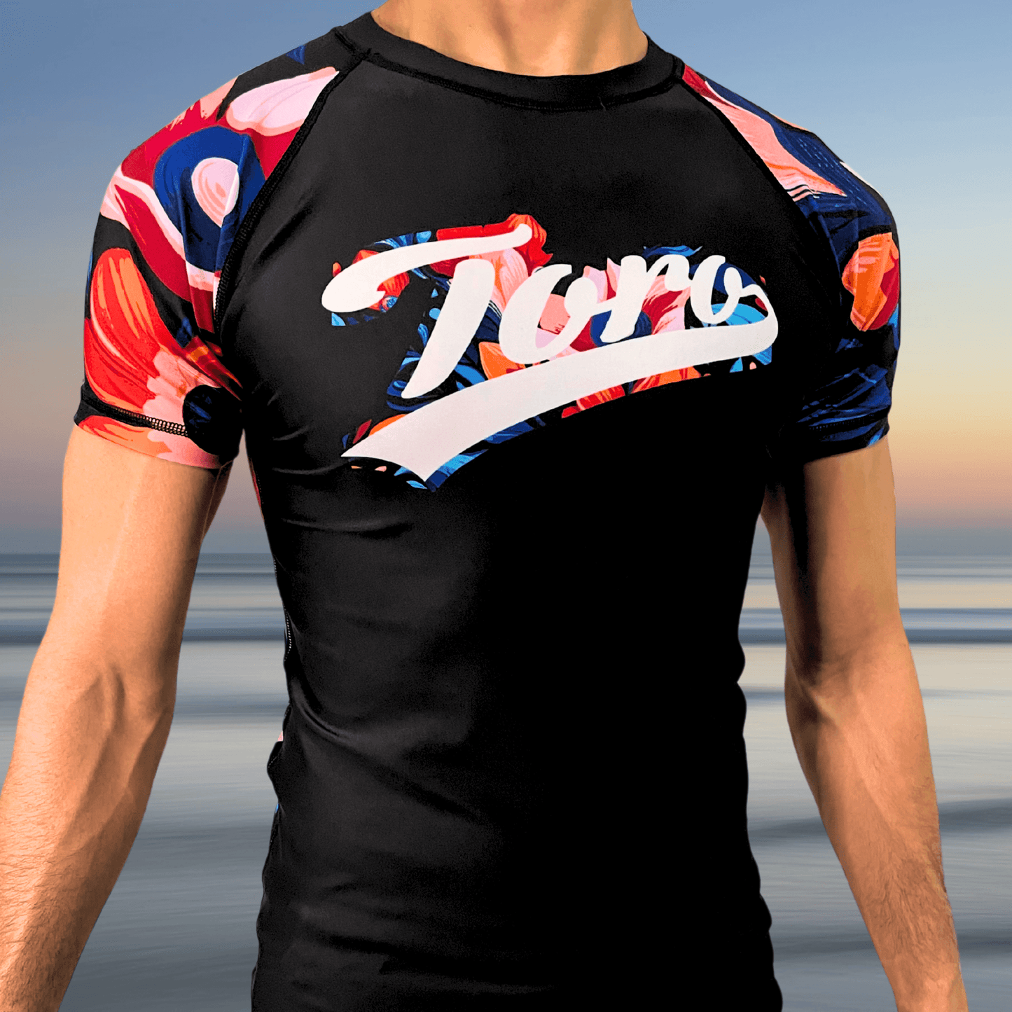 Front view of Toro BJJ Tiki Tahiti rash guard with floral-patterned sleeves and Toro script logo across the chest in tropical colors.