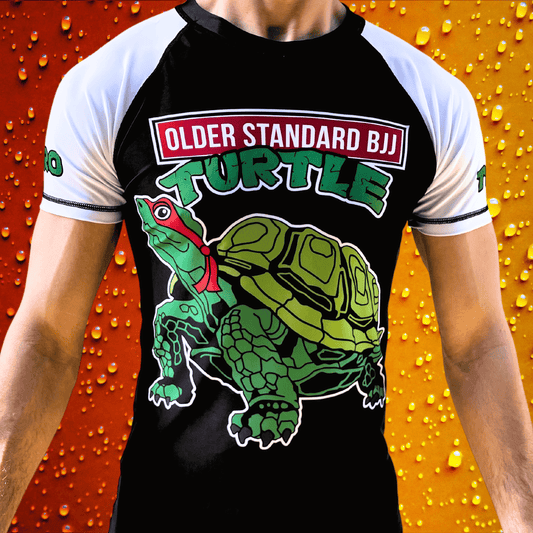 Person wearing the Toro BJJ Older Standard BJJ Turtle rash guard featuring a cartoon turtle graphic and "OLDER STANDARD BJJ" text across the chest.