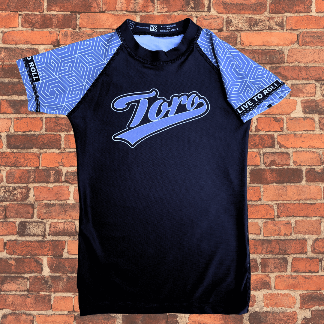 Toro BJJ Youth Gray Belt Rank Rash Guard featuring light blue geometric sleeve pattern, Toro script chest logo, and “Live to Roll” printed on the right arm.