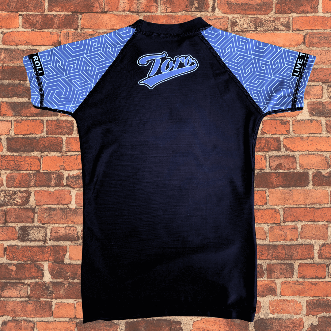Back view of the Toro BJJ Youth Gray Belt Rank Rash Guard with light blue patterned sleeves, black body, and Toro script logo centered between the shoulders.