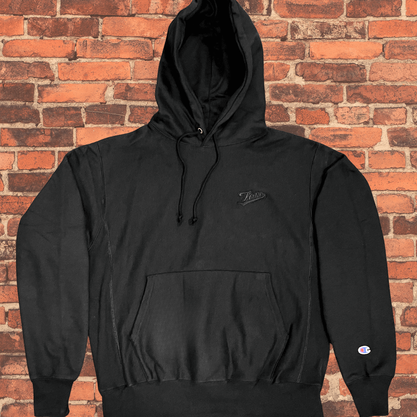 Toro x Champion Reverse Weave Hoodie black on black flat lay with embroidered Toro logo and Champion cuff patch.