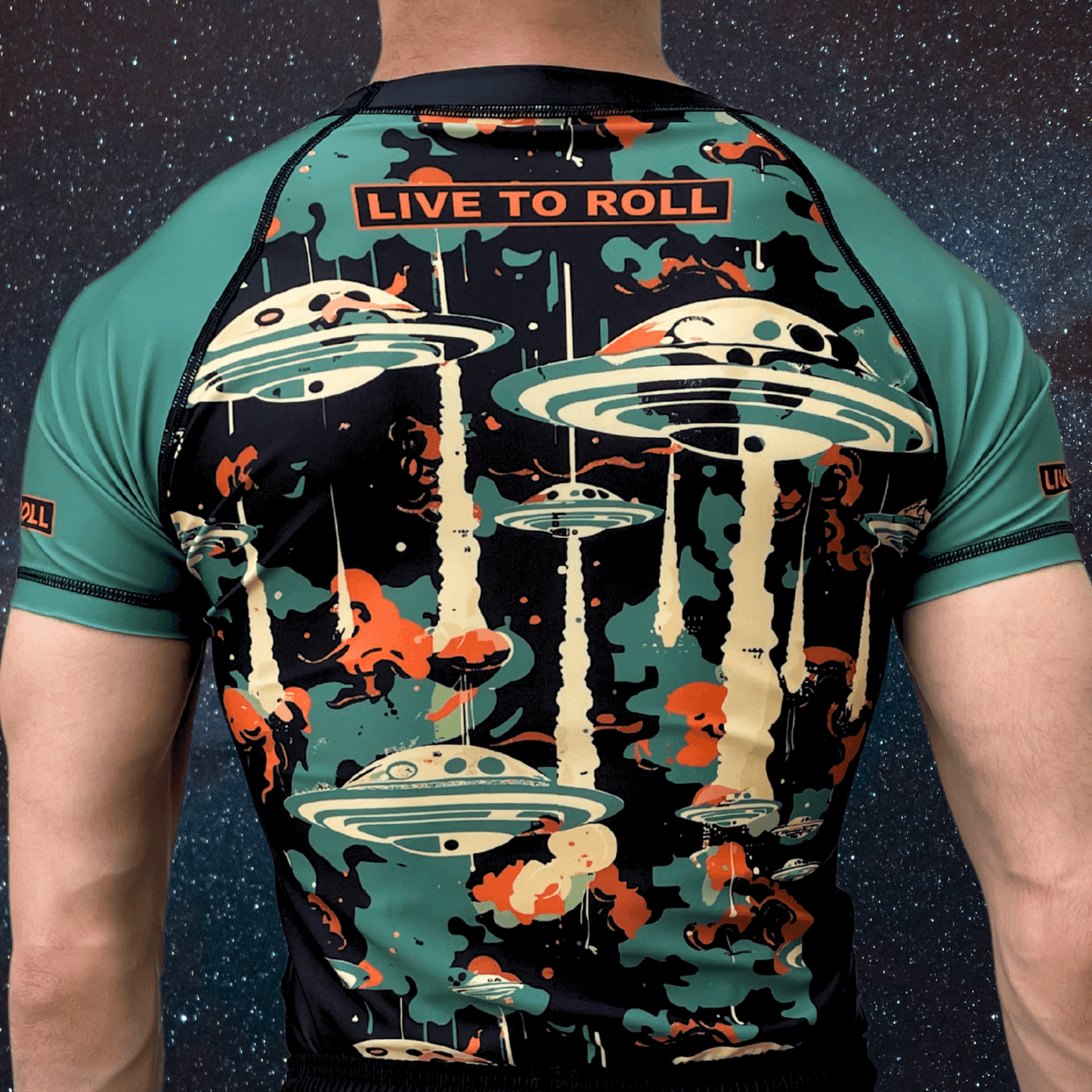 Back view of Toro BJJ Cosmic Rash Guard with “Live to Roll” text and UFO design in green, orange, and black tones