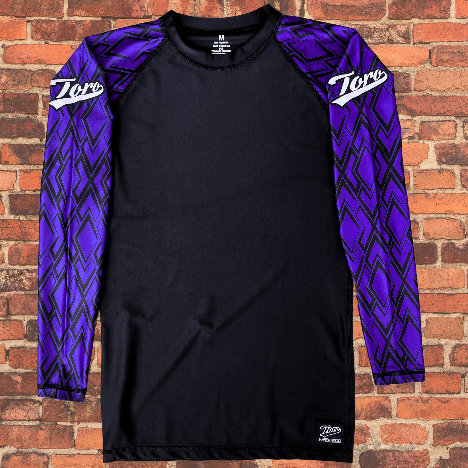 A long-sleeve BJJ rash guard with a black body and purple geometric-patterned sleeves, featuring the white "Toro" logo on both shoulders.