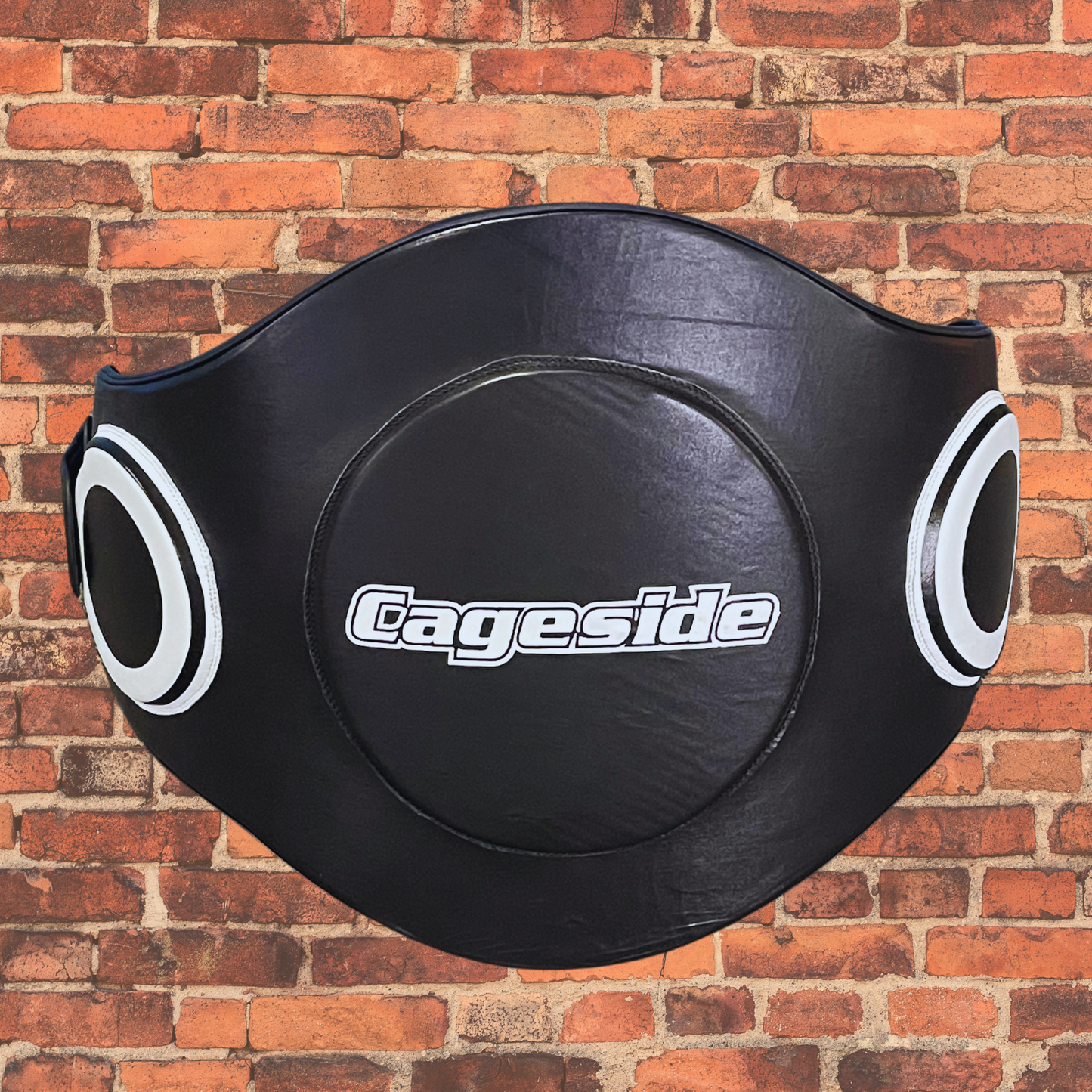 Image of Cageside's black protective body pad displayed against a red brick background. The body pad features reinforced circular target zones on the sides and a large center target, providing durability and impact resistance for MMA and combat sports training.