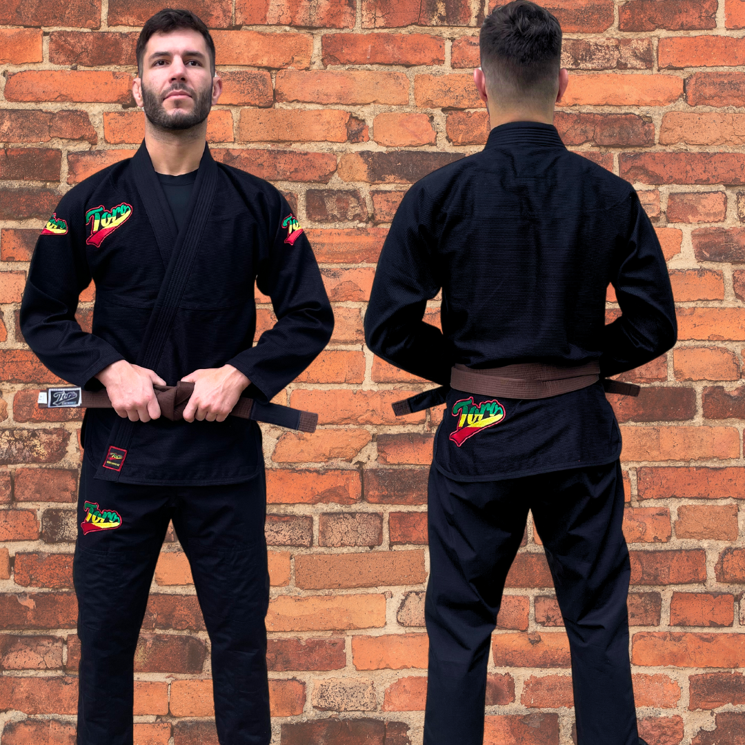 Man wearing Toro's black BJJ Gi with Rasta logos on chest, shoulders, and back. Paired with a brown belt.