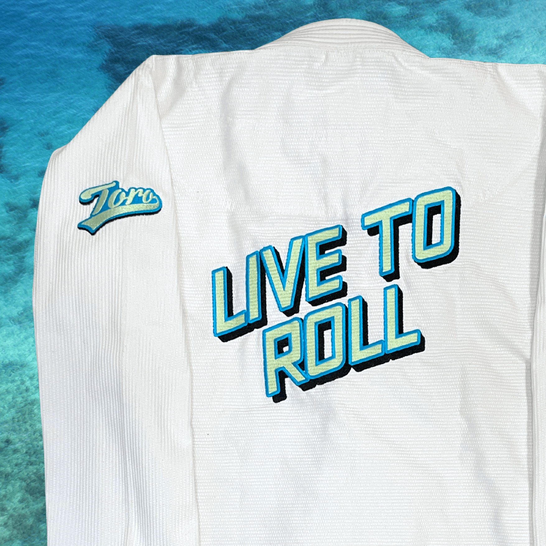 Close-up of Live to Roll embroidery and Toro logos on the back of the white Good Vibes BJJ Gi