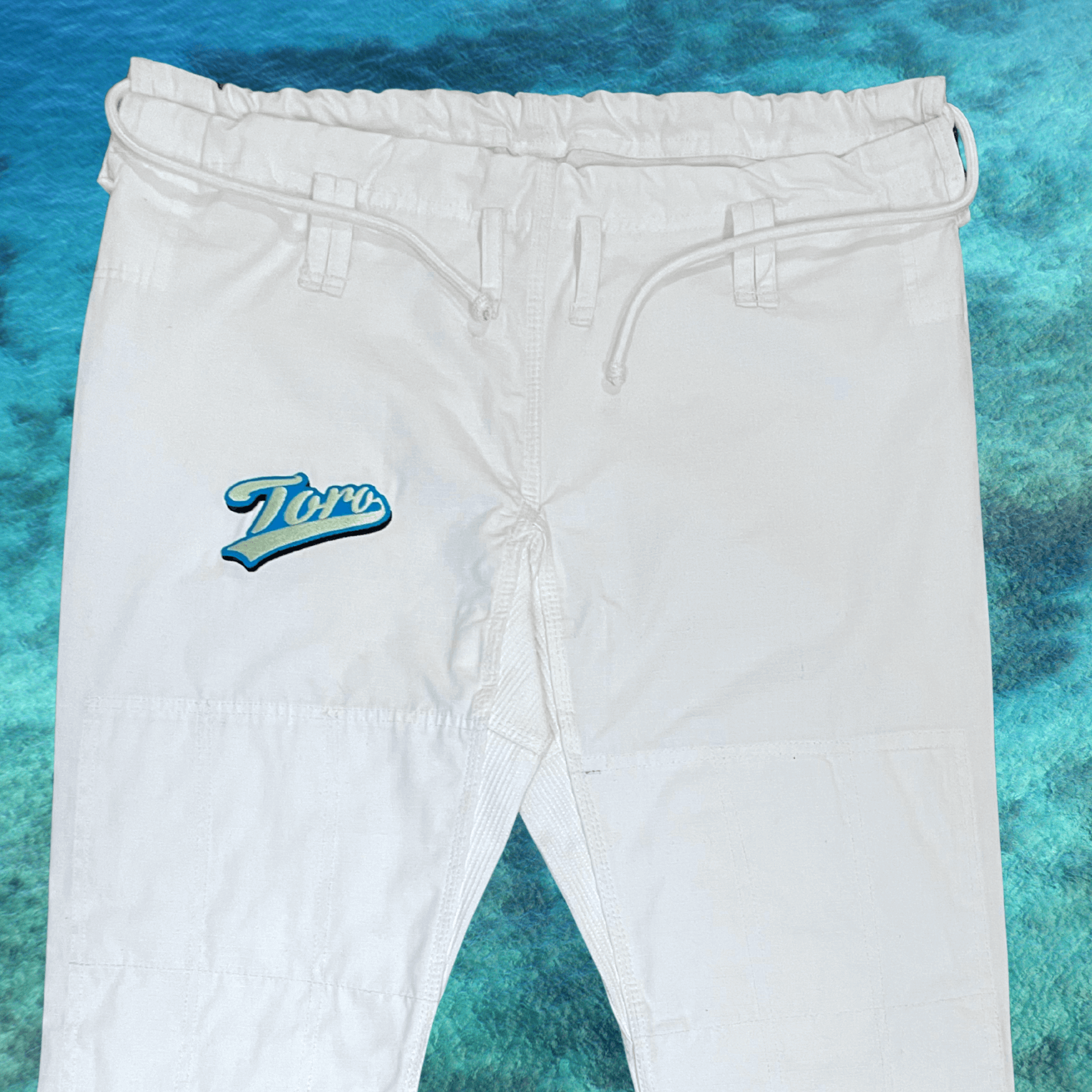 Close-up of Toro logo embroidery on white ripstop pants from the Good Vibes BJJ Gi
