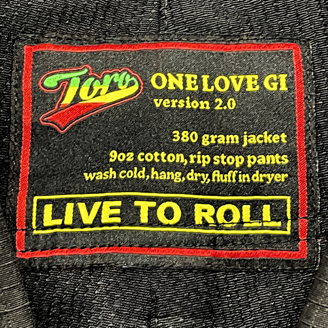 Close-up of Toro 'One Love Gi' v2.0 patch on durable 380g jacket & 9oz ripstop pants. 'Live to Roll' slogan in bold yellow.