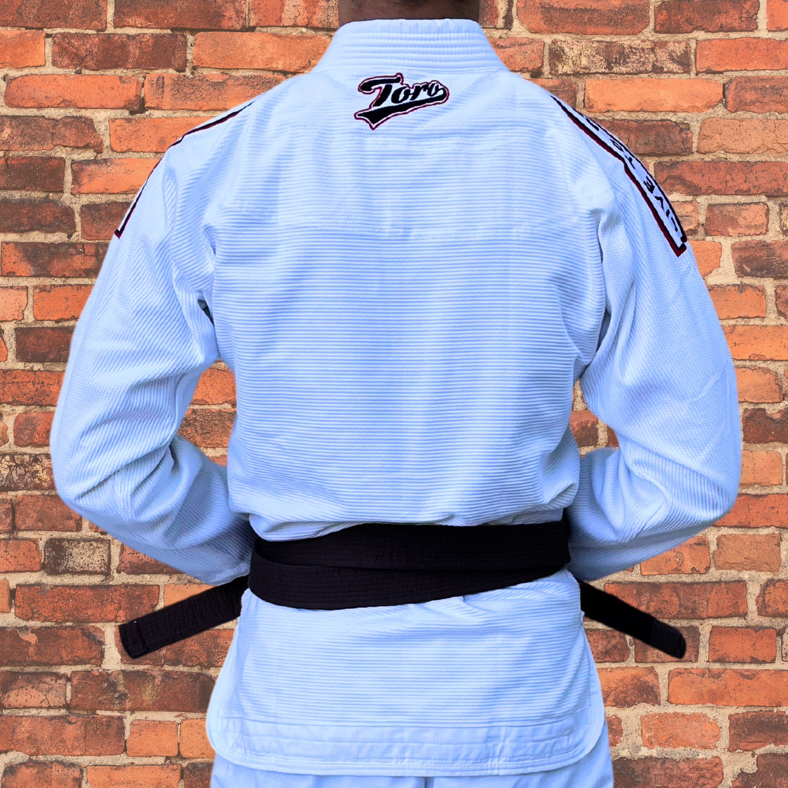 Back view of a Brazilian Jiu-Jitsu practitioner wearing a white Toro BJJ gi with a brown belt, showcasing the embroidered Toro logo on the upper back and shoulder patches. The gi offers a lightweight, durable design ideal for training and competition.
