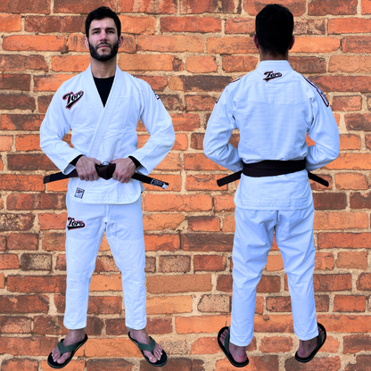 Front and back view of a man wearing Toro's white BJJ Gi with a brown belt, standing against a red brick wall backdrop. The Gi features the Toro logo on the chest, pants, and back, offering a clean and lightweight design perfect for Brazilian Jiu-Jitsu athletes. Durable and comfortable for both training and competition.
