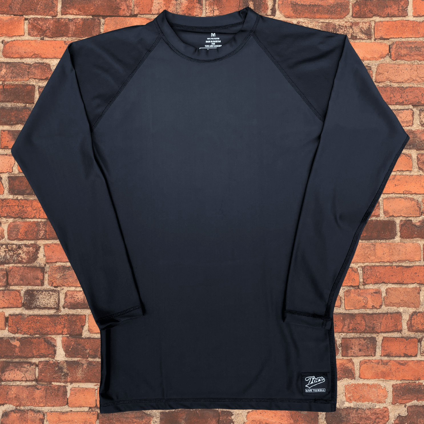 Toro Youth Black Label Long Sleeve BJJ Rash Guard laid flat on brick background showing front design