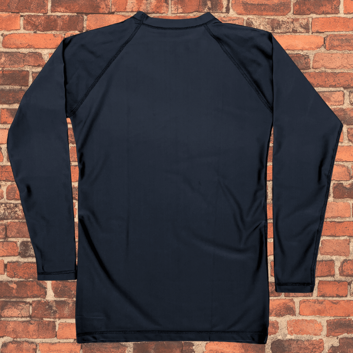 Toro Youth Black Label Long Sleeve BJJ Rash Guard laid flat on brick background showing back panel and stitching