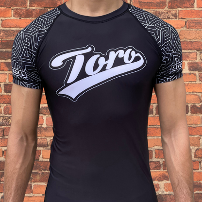 Man wearing a Toro black belt ranked rash guard with black geometric sleeve design.