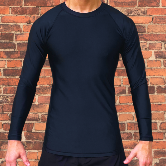 Man wearing a black long sleeve rash guard, standing against a brick wall. 