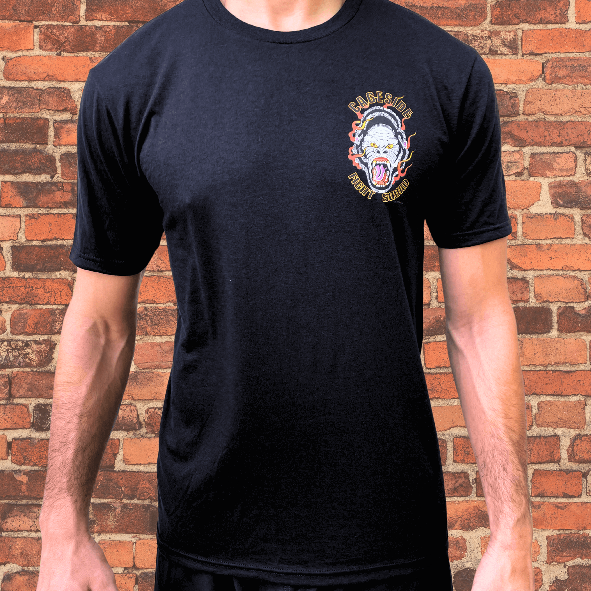 Black Cageside Fight Squad t-shirt with flaming gorilla logo on chest, modeled against brick wall background