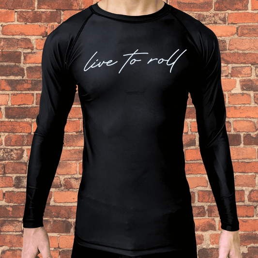 Black long-sleeve rash guard with "live to roll" script across the chest, worn by a male model standing in front of a brick wall.