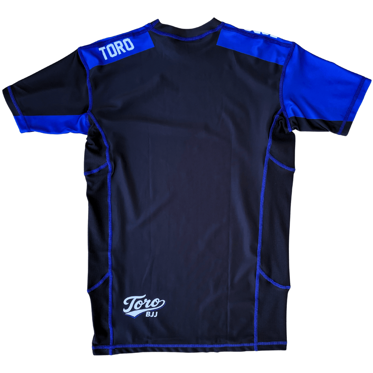 Back view of Toro 2027 blue belt rash guard with blue shoulder panels and a white lower back logo
