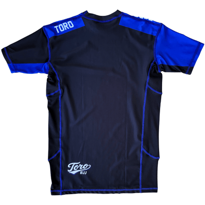 Back view of Toro 2027 blue belt rash guard with blue shoulder panels and a white lower back logo