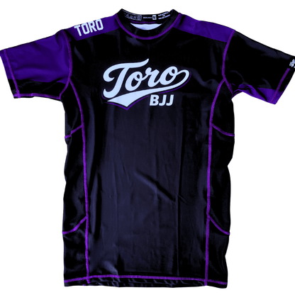 Front view of Toro 2027 purple belt rash guard with a black body, purple accents, and white chest logo