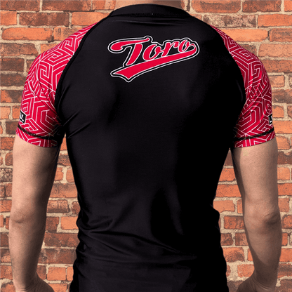 Back view of Toro BJJ Black Belt Ranked Rash Guard with black body, red geometric pattern sleeves, Toro logo across upper back.