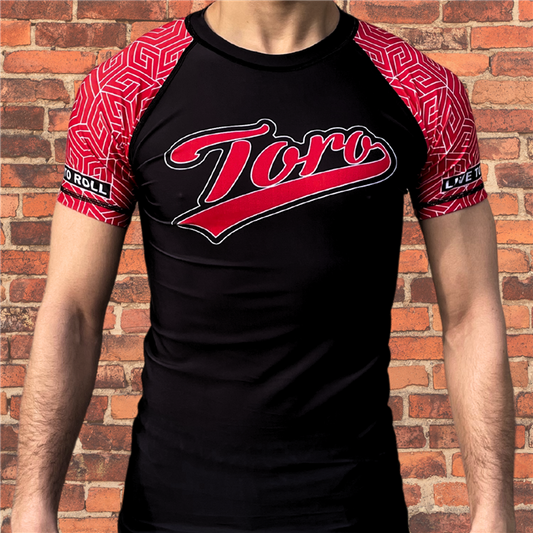 Toro BJJ Black Belt Ranked Rash Guard with black body, red geometric pattern sleeves, Toro logo across chest, Live to Roll patch on sleeve.