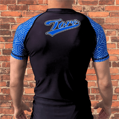 Back view of Toro BJJ Blue Belt Ranked Rash Guard with black body, blue geometric pattern sleeves, and bold Toro logo across the upper back.