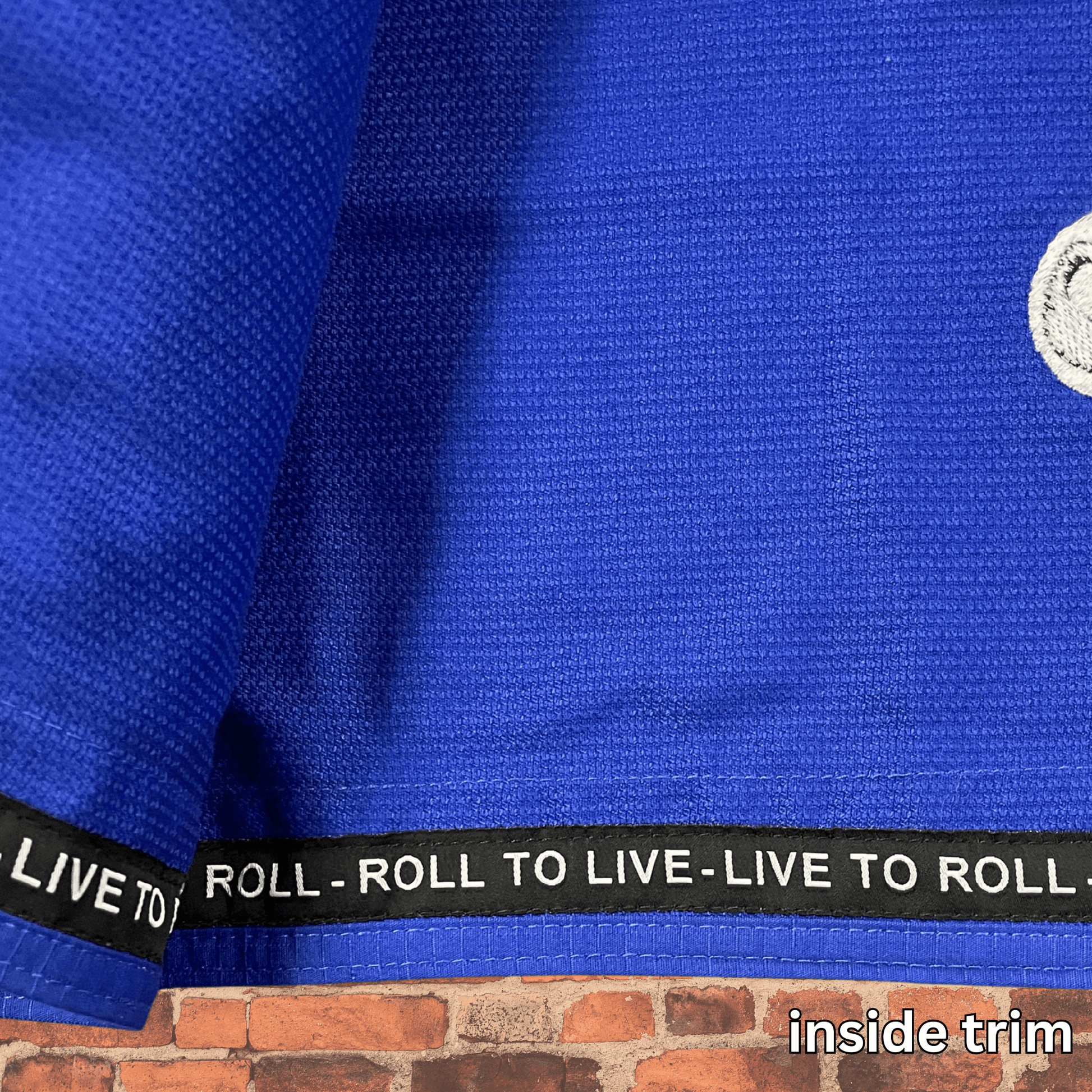 Close-up of Toro BJJ Blue Bull women’s cut gi inside trim, black with "Live to Roll – Roll to Live" text, on blue gi fabric with contrast stitching.