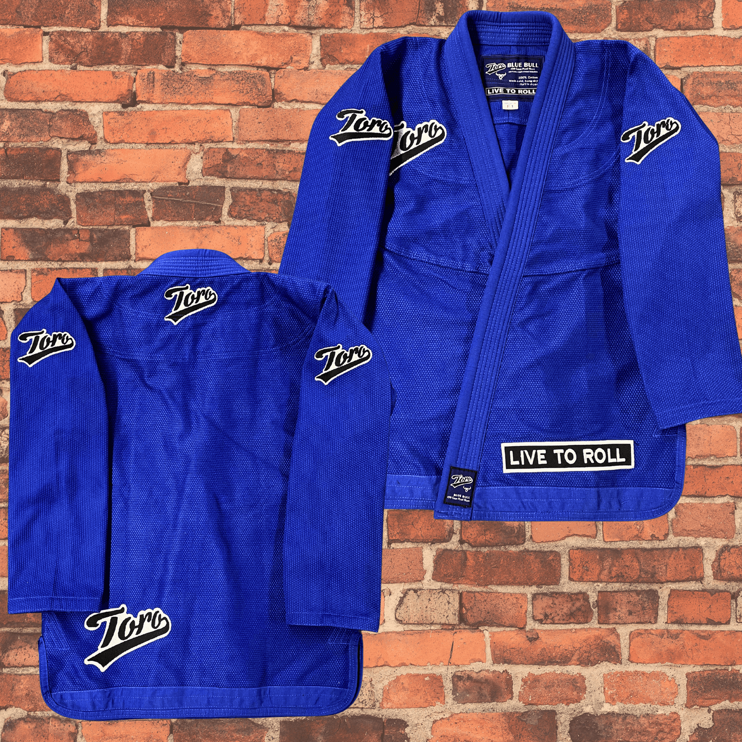Toro BJJ Blue Bull women’s cut BJJ gi jacket, bold Toro logos on chest, sleeves, back, and “Live to Roll” patch on lapel, shown on brick background.