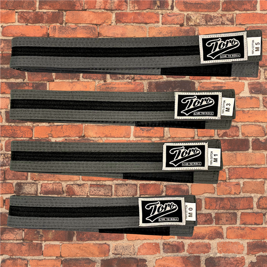 Toro BJJ kids gray and black BJJ belts in sizes M0–M5, featuring Toro logo patch with 'Live to Roll' text, black rank bar, brick background.