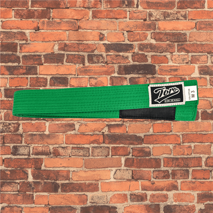 Toro BJJ kids solid green BJJ belts in sizes M000–M5, Toro logo patch with 'Live to Roll' text beneath, black rank bar, brick background.