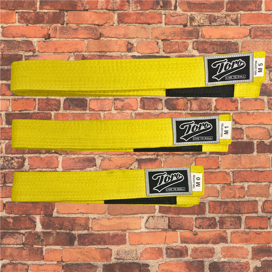 Toro BJJ kids yellow BJJ belts in sizes M0–M5, featuring black rank bars and Toro logo patches, displayed on brick background.