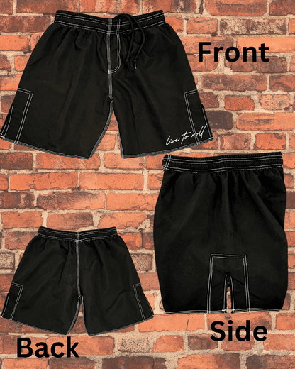 Black Toro BJJ 'Live to Roll' shorts displayed flat against a brick wall, showing front, back, and side views with white stitching and 3-inch side slits.