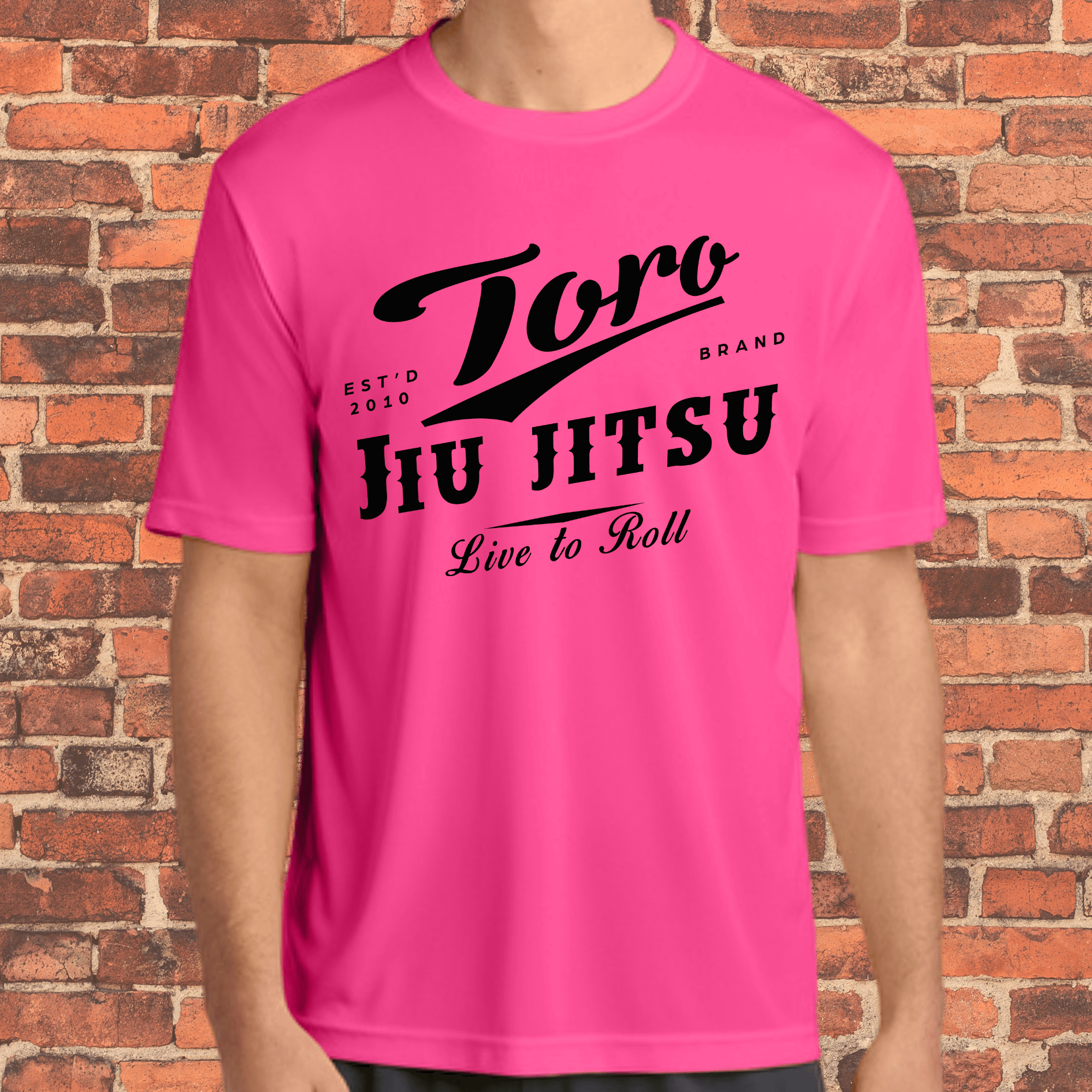 Adult-sized neon pink loose fit rash guard with bold black Toro Jiu Jitsu "Live to Roll" design, worn by a model in front of a brick wall.