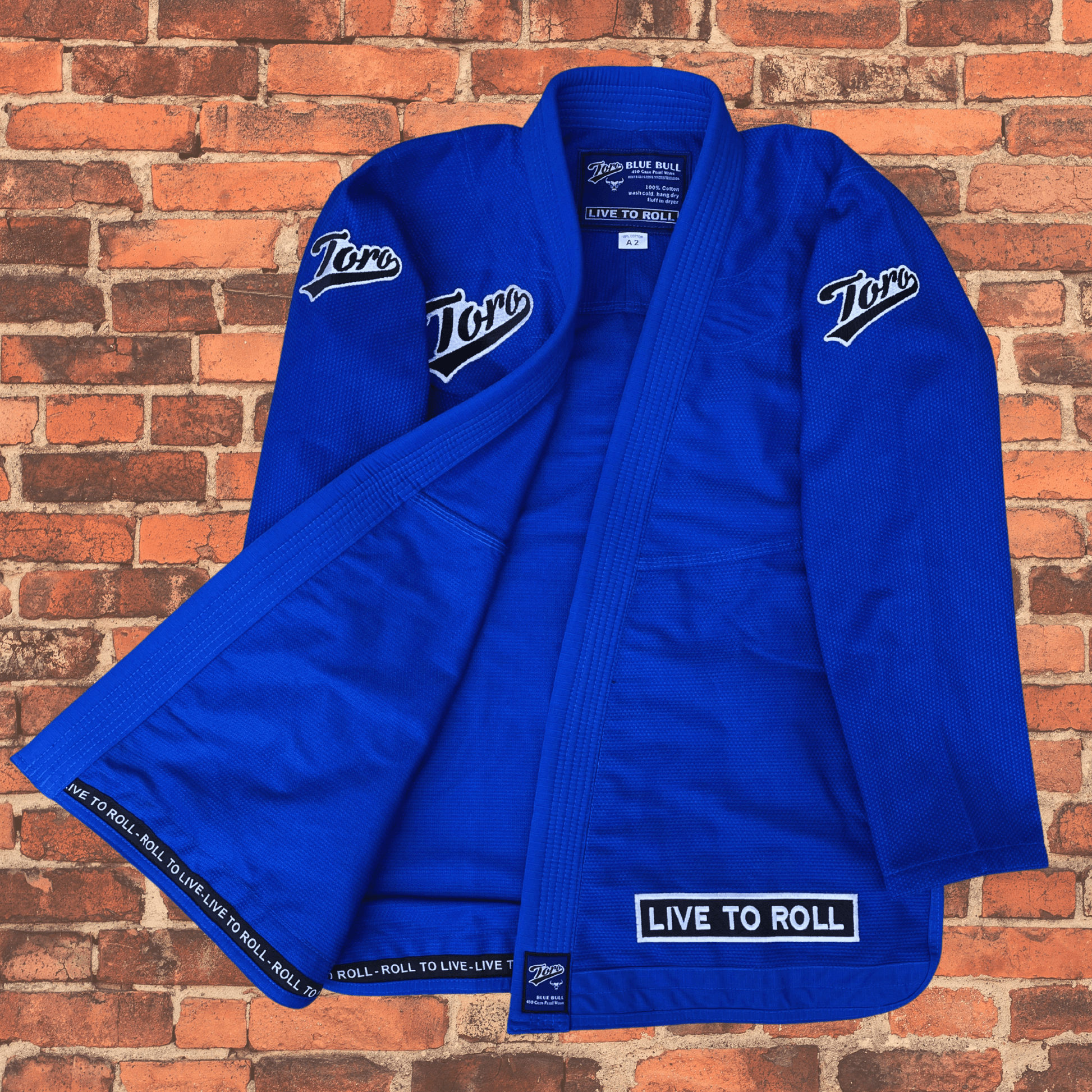 Toro BJJ Men’s Blue Bull Gi jacket open to show inside trim with “Live to Roll” text, blue fabric, Toro patches on chest and sleeves.